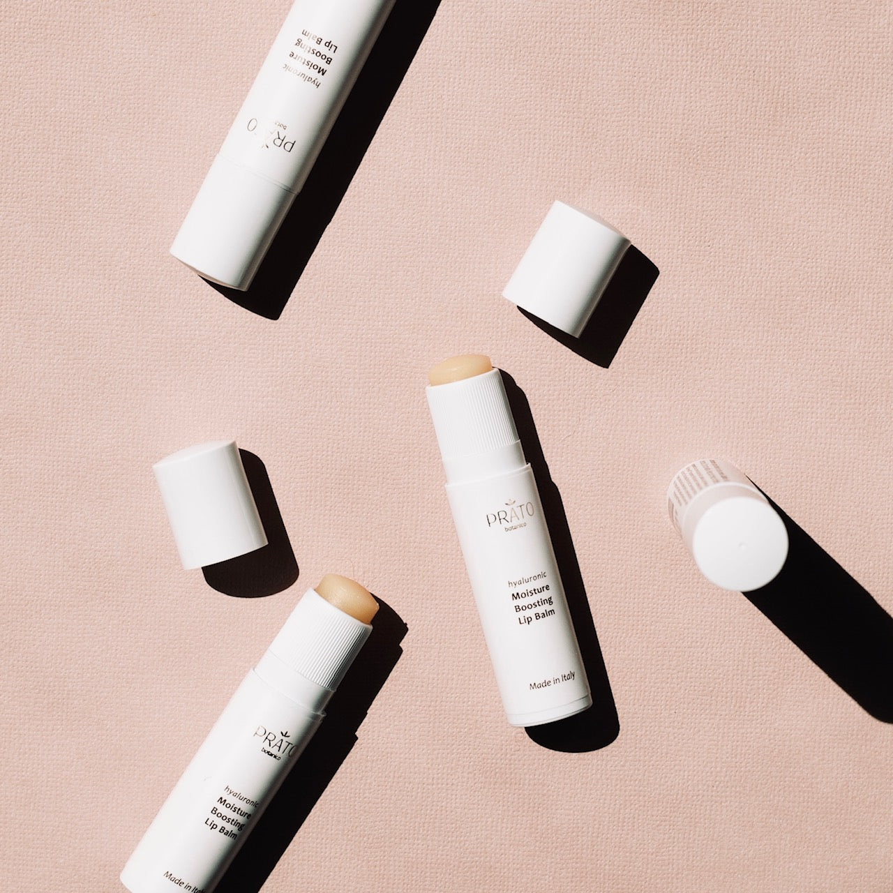 Array of Prato Botanico Moisture Boosting Lip Balms with lids removed on pink background