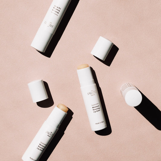 Array of Prato Botanico Moisture Boosting Lip Balms with lids removed on pink background